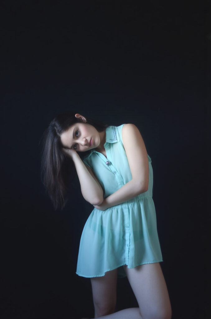 Mariana Esquivel poses elegantly against a dark backdrop wearing a light blue sleeveless dress with a unique collar design.